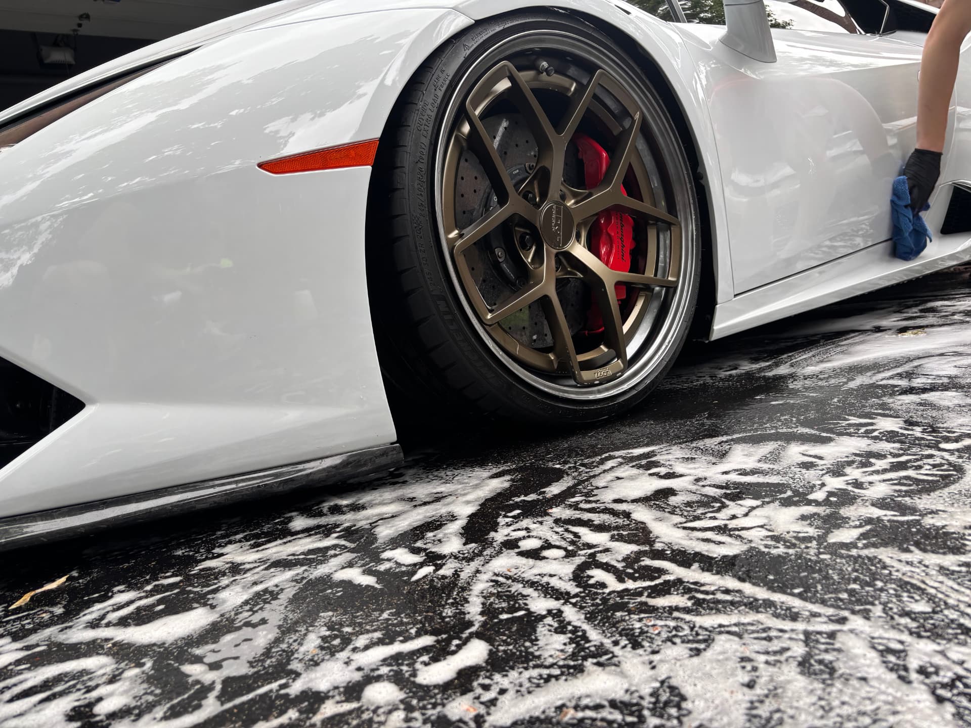 Detailer wiping a white Lamborghini beside a bronze wheel and red brake caliper mid-wash