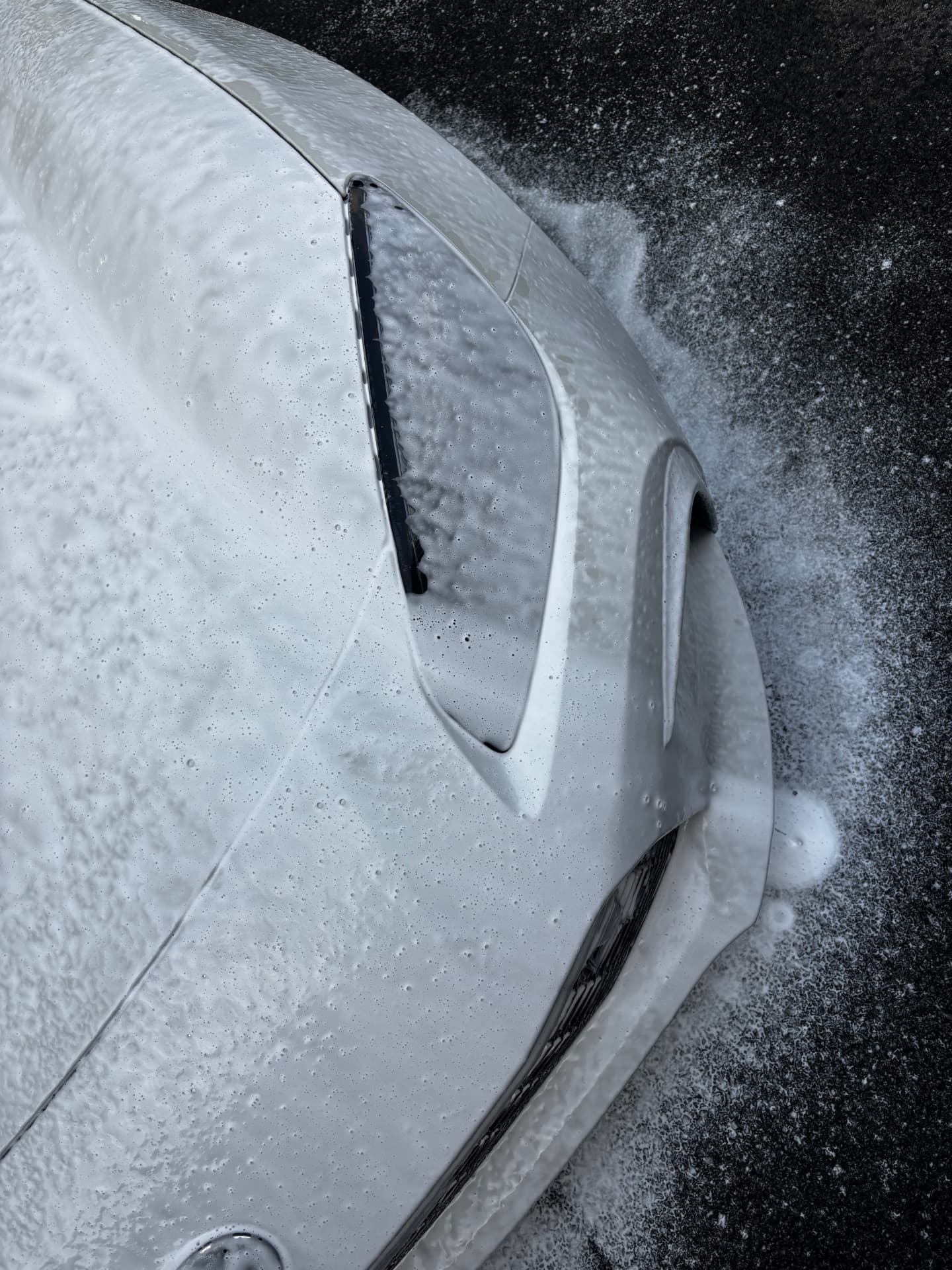 Hood and front bumper of a white car covered in thick foam during a hand wash