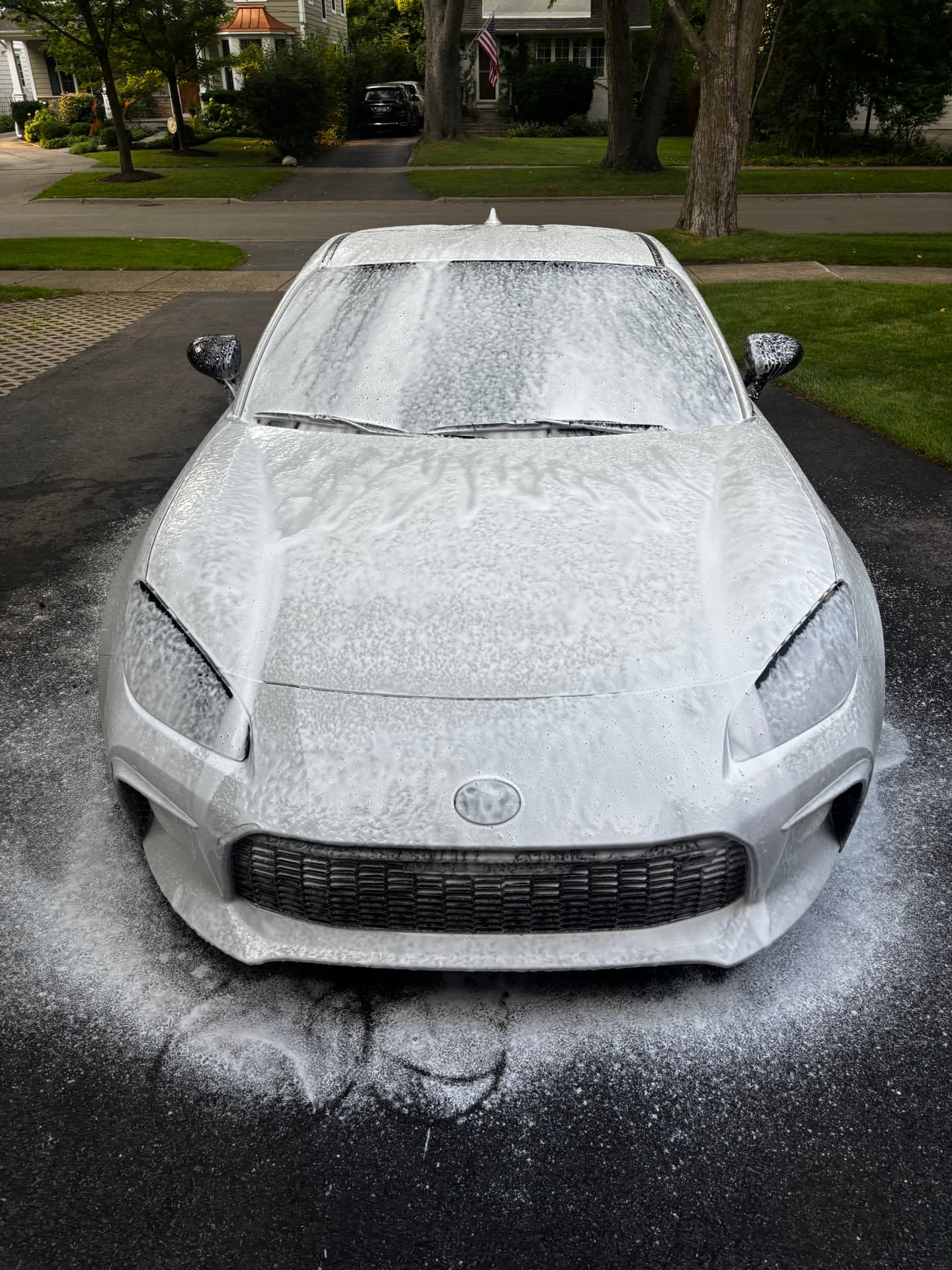 White Toyota GR86 covered in thick foam in a driveway during a hand wash